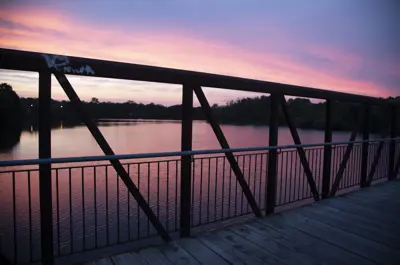 Railing of footbridge overlooking river at sunset