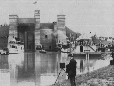 Historical photo, photographer on shoreline in foreground, hydraulic lift lock in background on a canal
