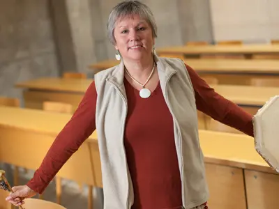 A person standing, holding a drum in one hand